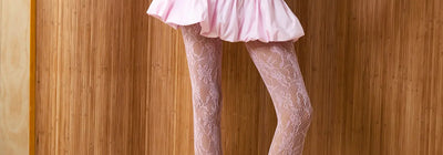Person wearing a pink dress and fishnet stockings against a wooden paneled wall.